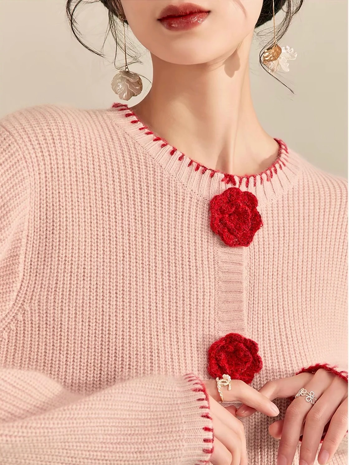 Detail Rosette Cardigan: kerah bulat dengan jahitan tepi merah dan kancing mawar rajut merah.