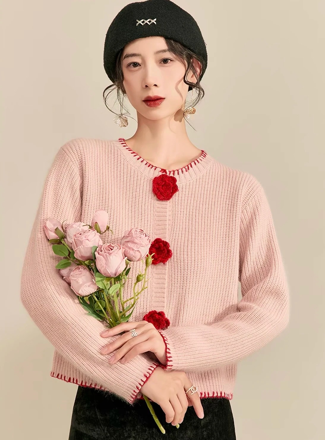 Perempuan berbaret hitam memakai Rosette Cardigan yang dikancingkan, membawa mawar pink.