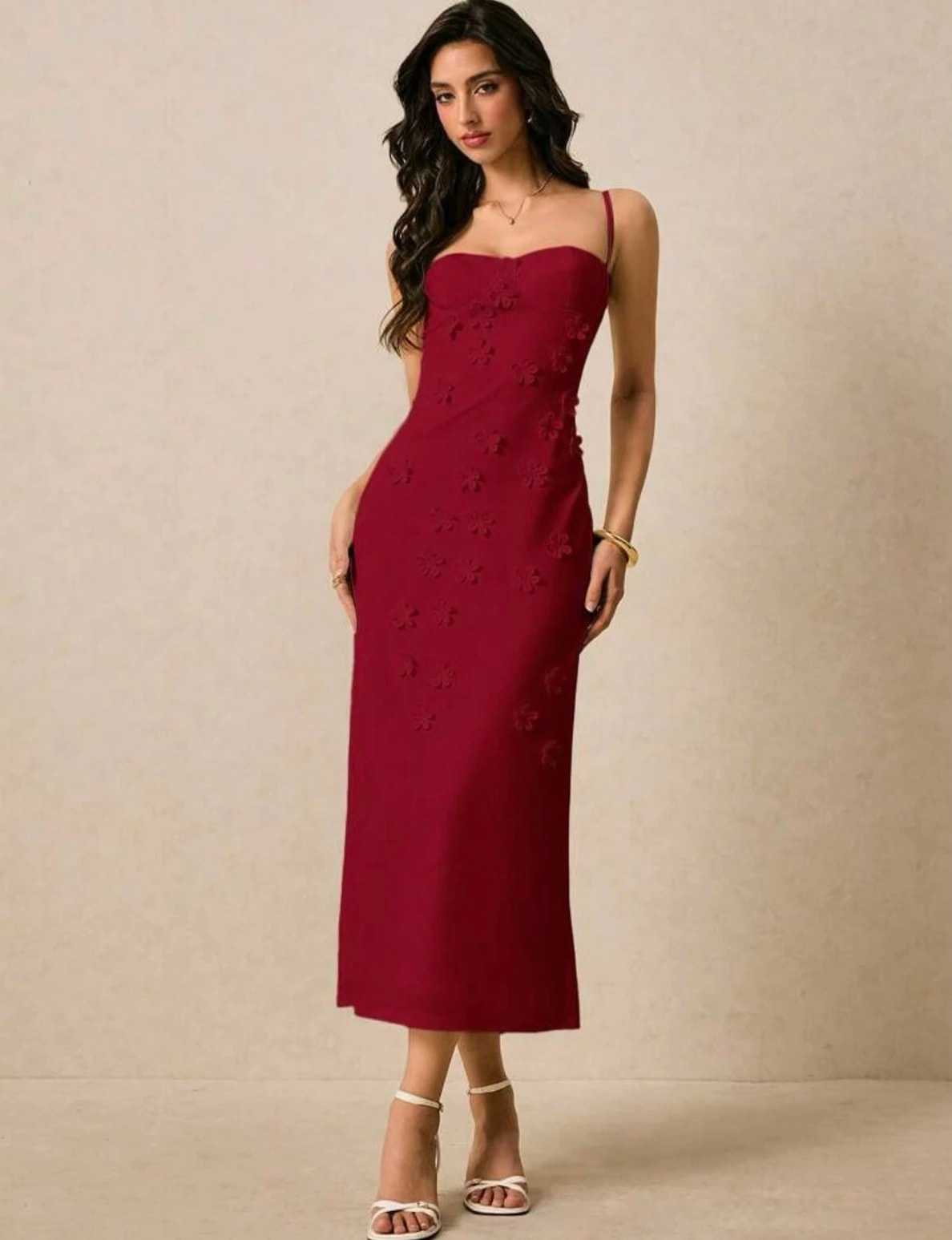 Perempuan memakai Adele Dress warna burgundy, baju pesta Natal, dengan tali tipis, kerah bentuk hati, dan bunga kain timbul di rok midi lurus.