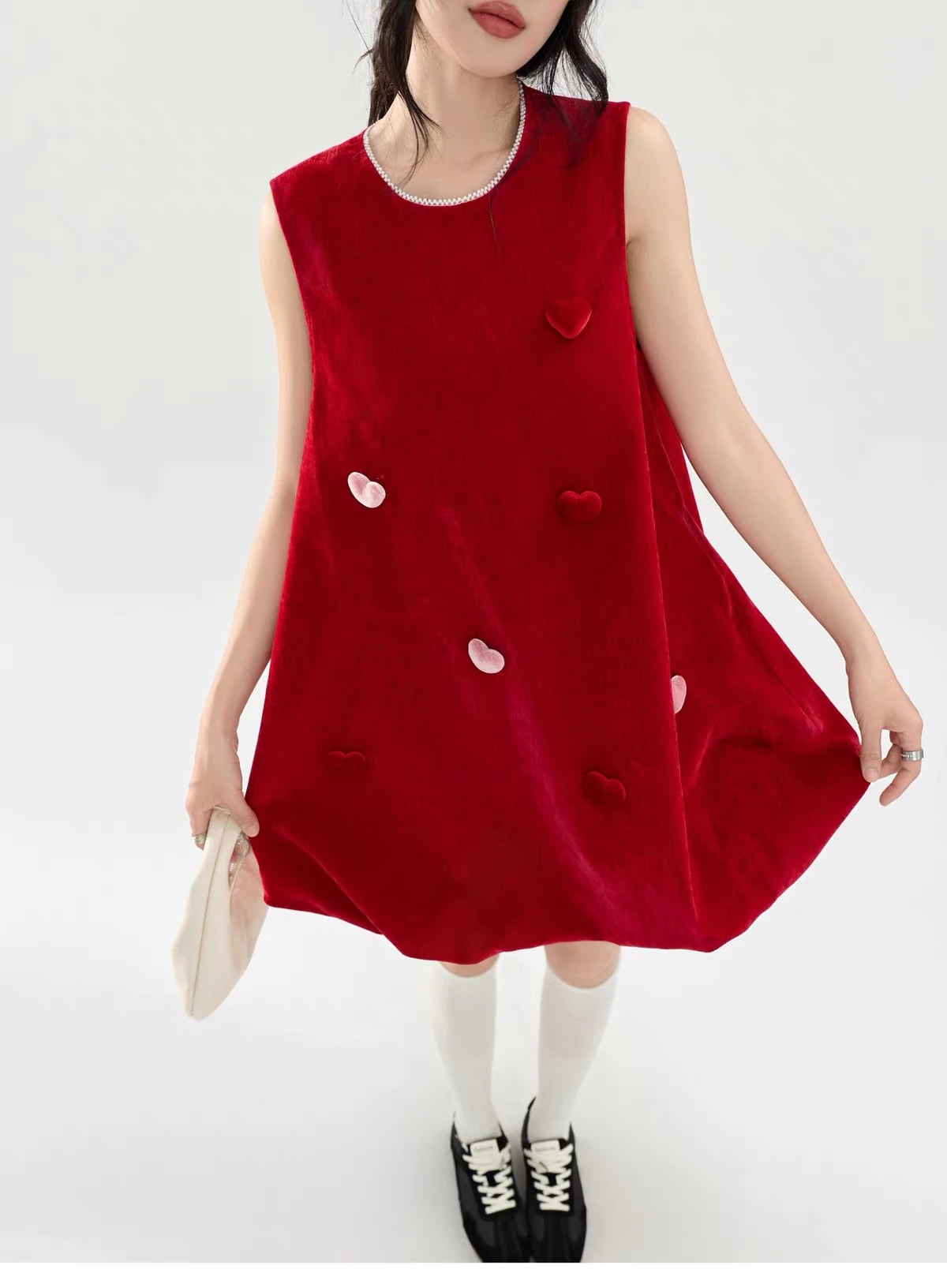 A woman holding out the skirt of the Cerise Dress, showing the soft velvet and the scattered red and pink hearts.