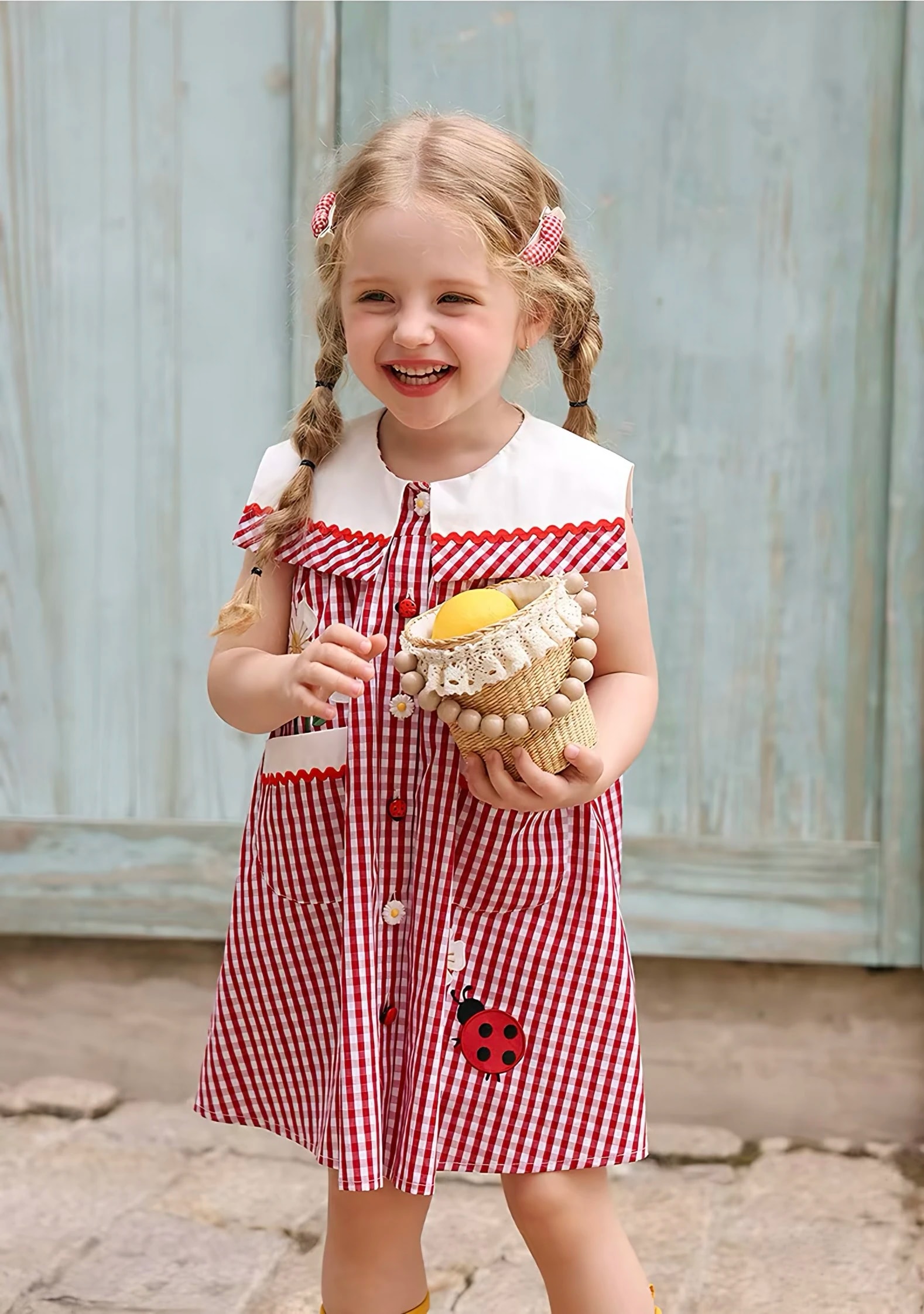 A laughing girl holding a basket in the Rosalie Dress, with the wide white collar and a ladybug appliqué in view.