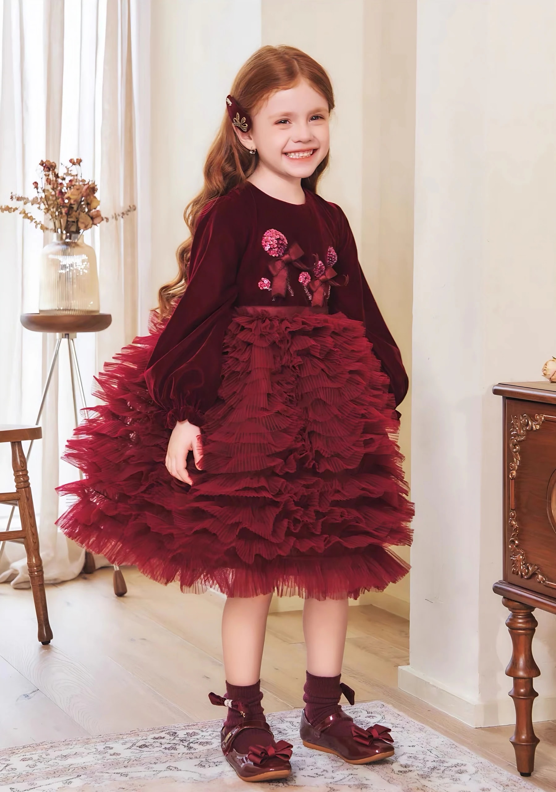 Tampak depan anak perempuan tersenyum memakai Eleonore Dress, terlihat hiasan bunga di atasan beludru dan rok tulle berlapis.