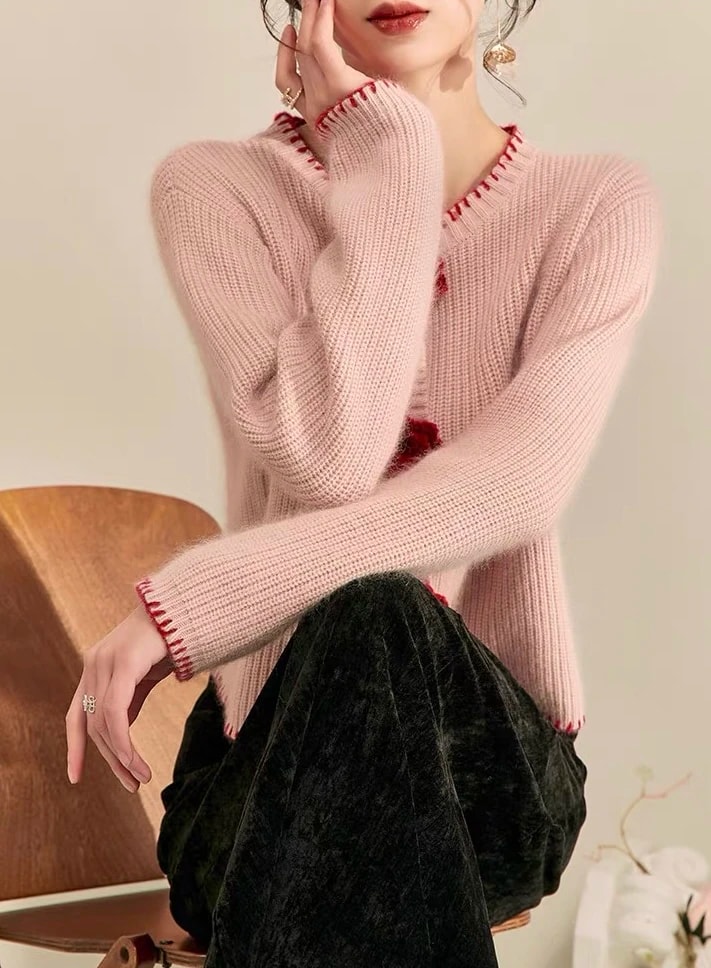 Pose duduk memakai Rosette Cardigan, terlihat lengan panjang rajut rib dan jahitan tepi merah di ujung lengan.