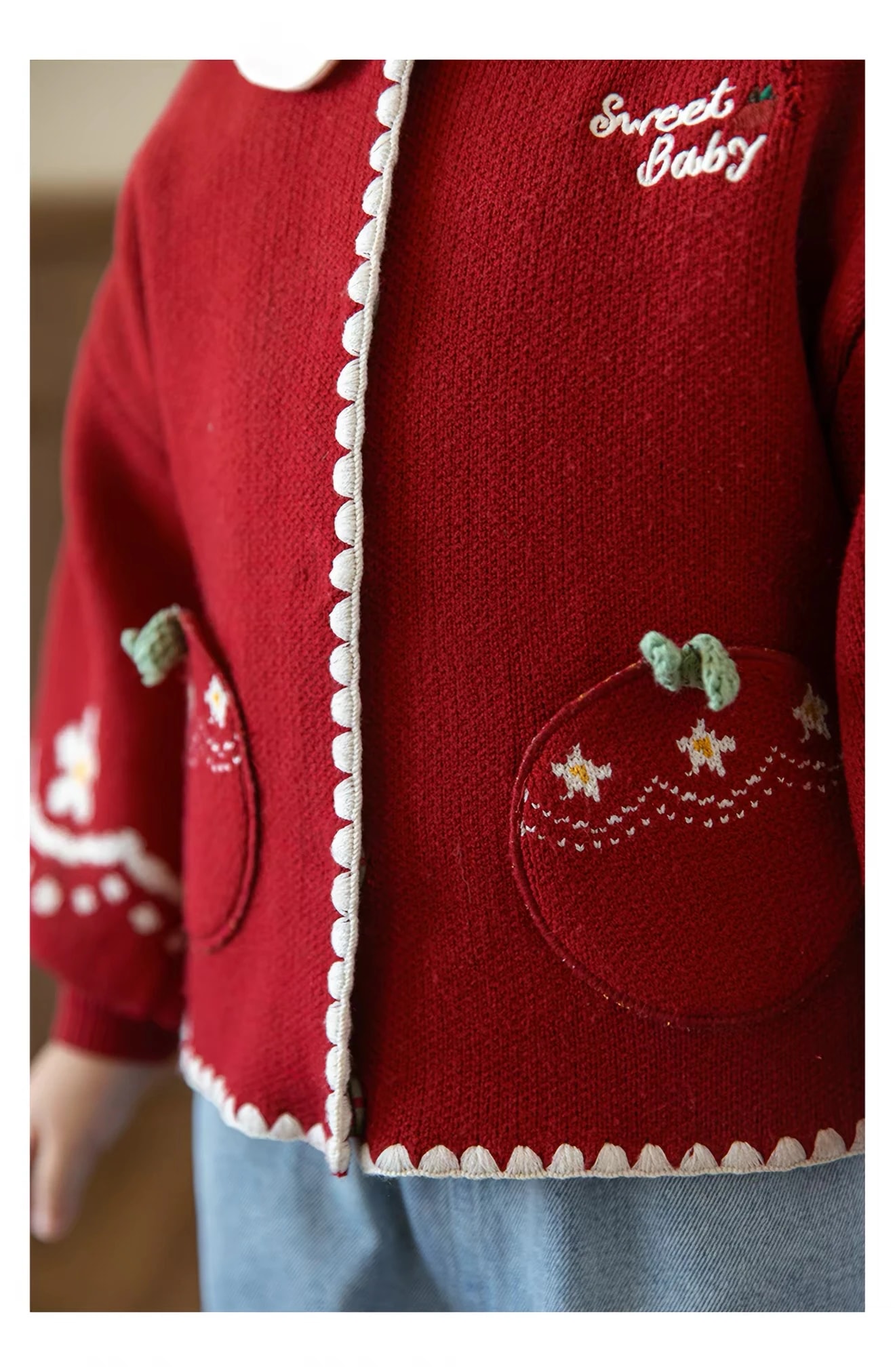 Detail Pomme Cardigan merah: saku apel dengan daun rajut, motif bintang, dan tepi bergelombang gading.