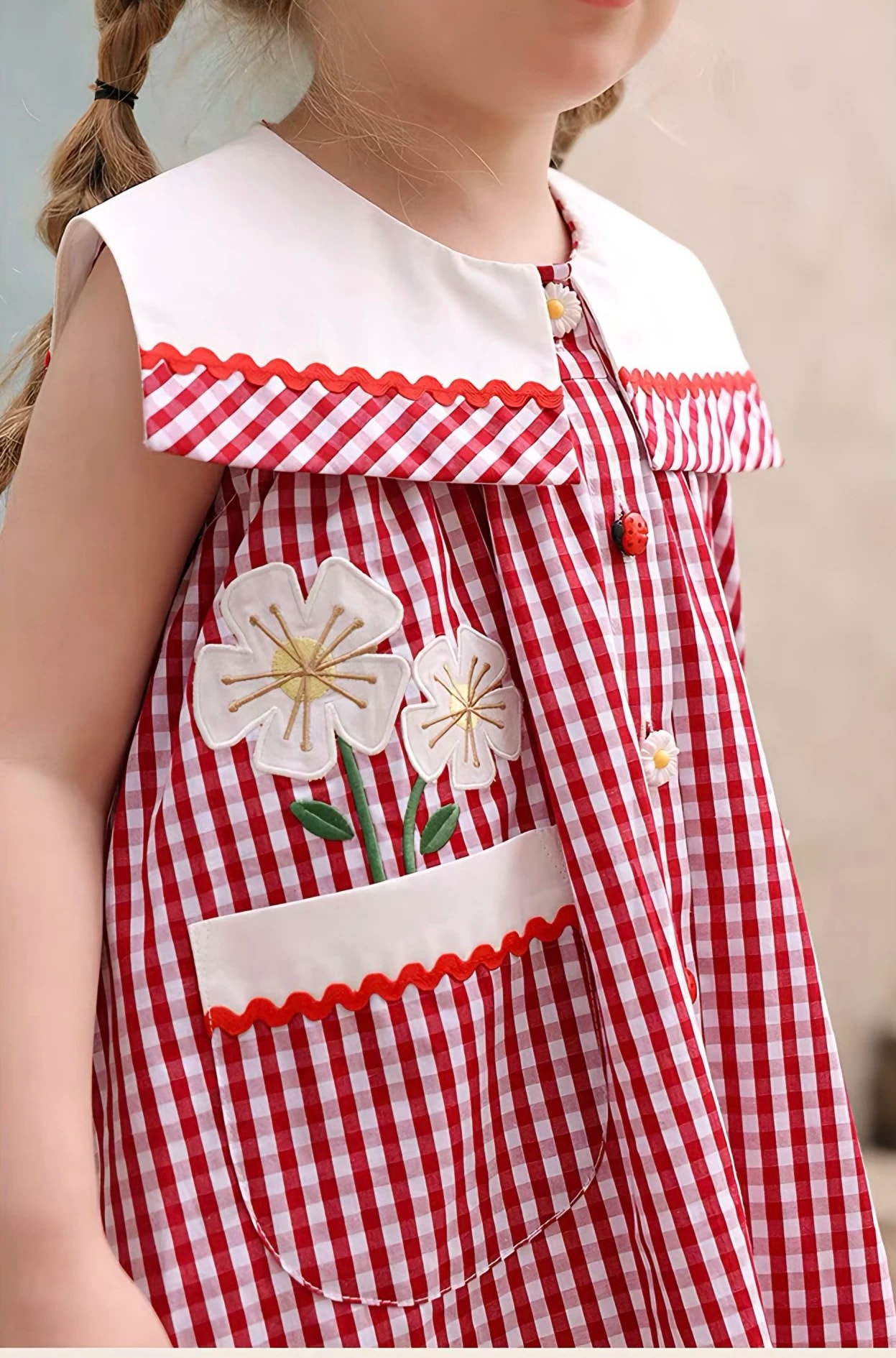 Detail Rosalie Dress: bordir bunga di atas saku tempel dengan list putih dan pita gelombang merah.