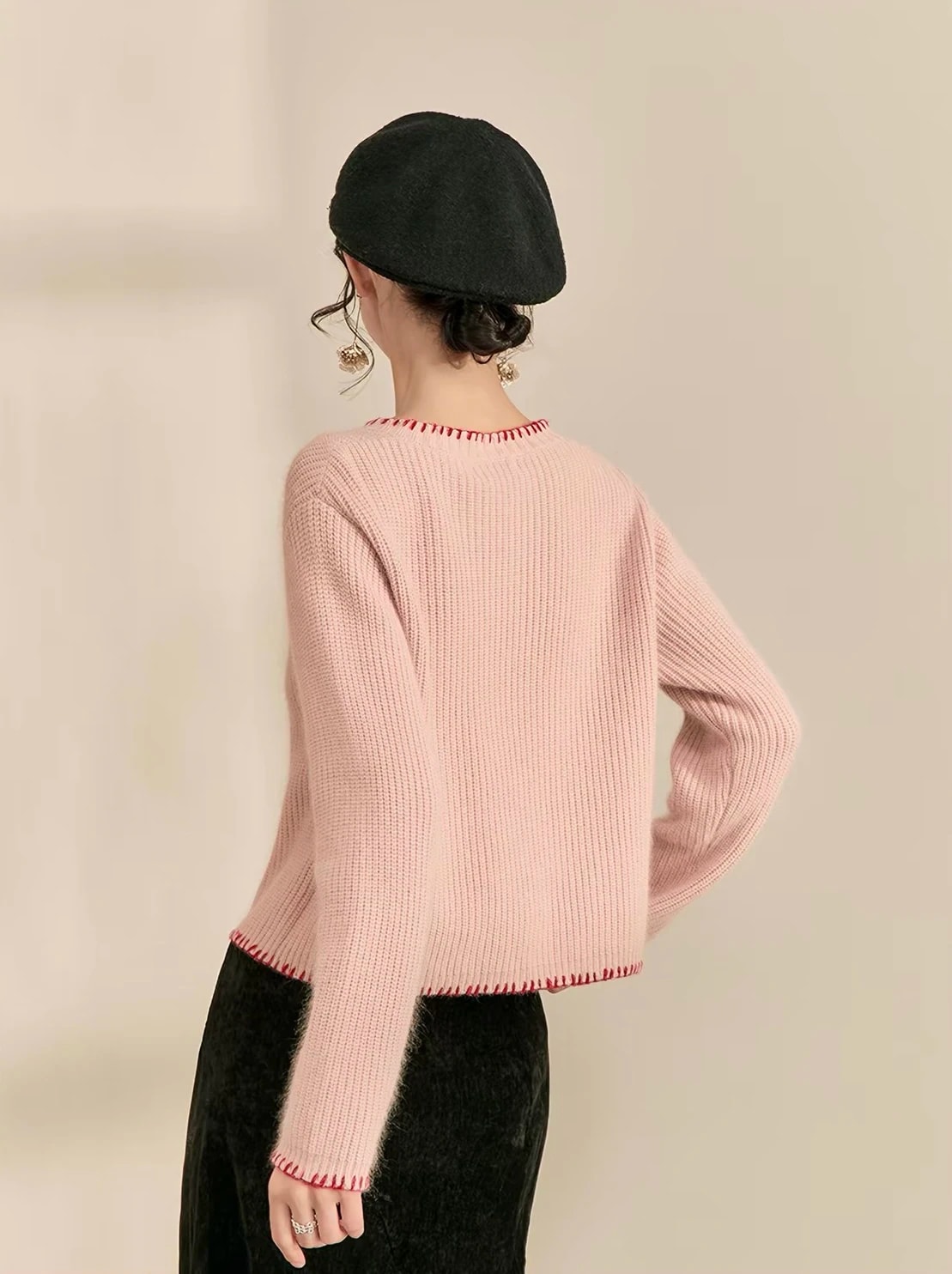 Tampak belakang Rosette Cardigan dengan jahitan tepi merah di kerah, ujung lengan, dan bagian bawah, dipadukan baret hitam.