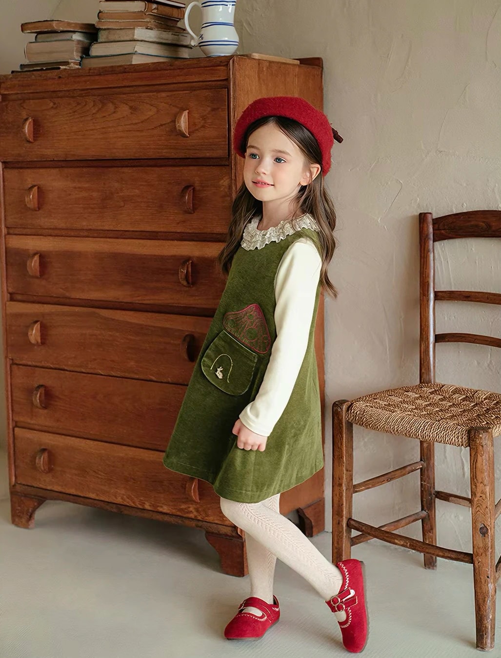 Anak perempuan berjalan memakai Madeleine Dress, tampak agak menyamping, terlihat sisi pinafore dan saku berbordir jamur.