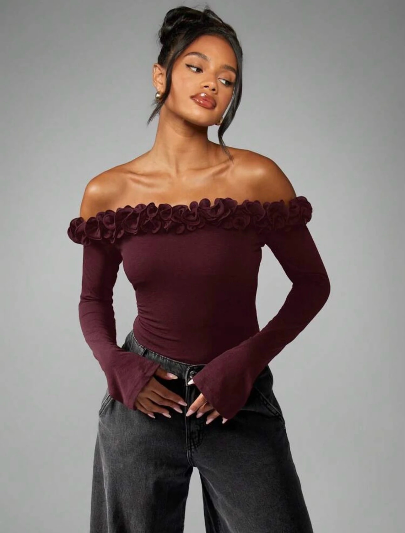 Perempuan memakai Roselia Top warna burgundy, baju Natal, dengan hiasan mawar kain di kerah sabrina dan lengan panjang melebar.