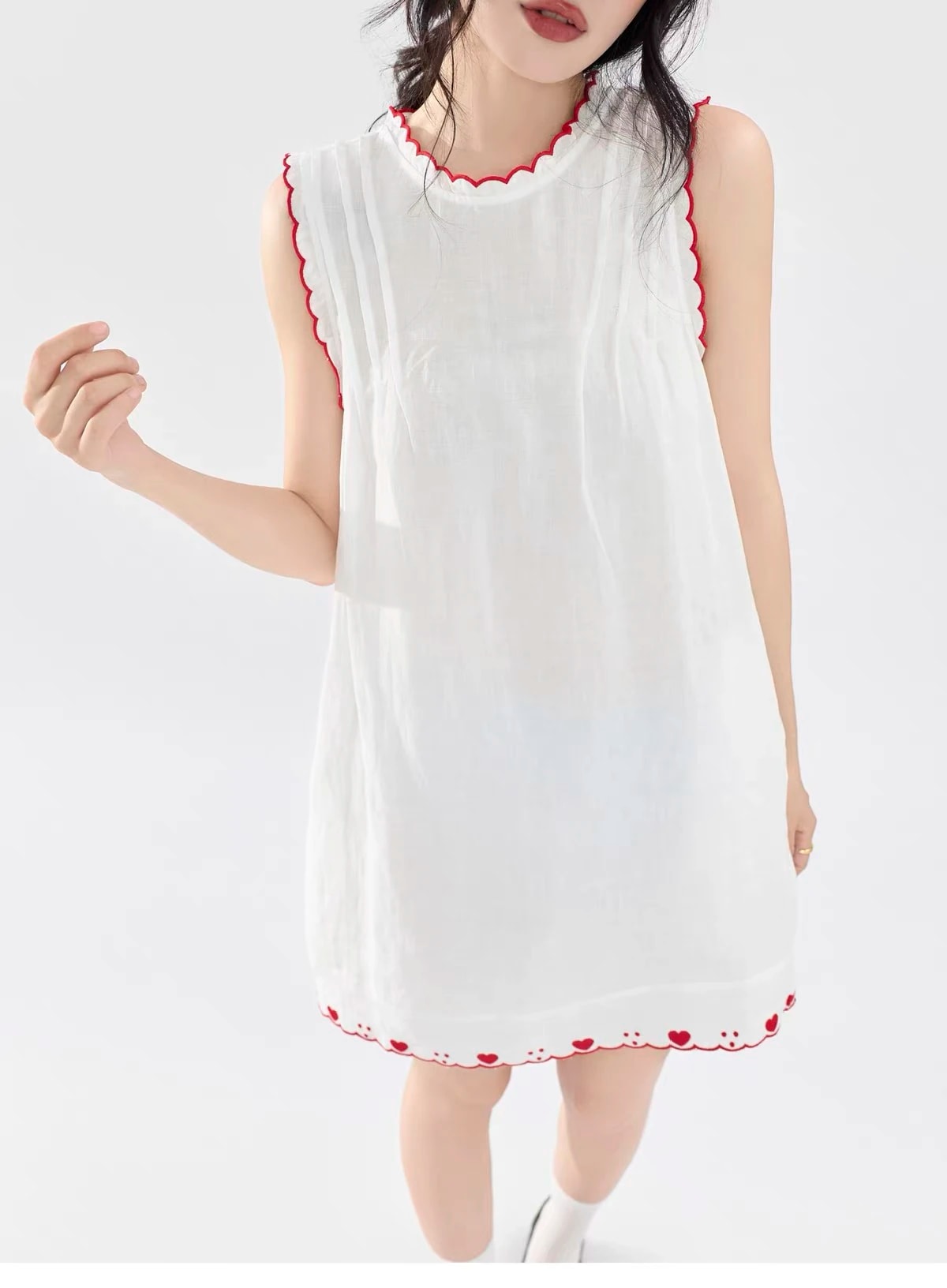 Front view of the white Lucie Dress, with red scalloped trim at the neck and armholes and red hearts along the hem.