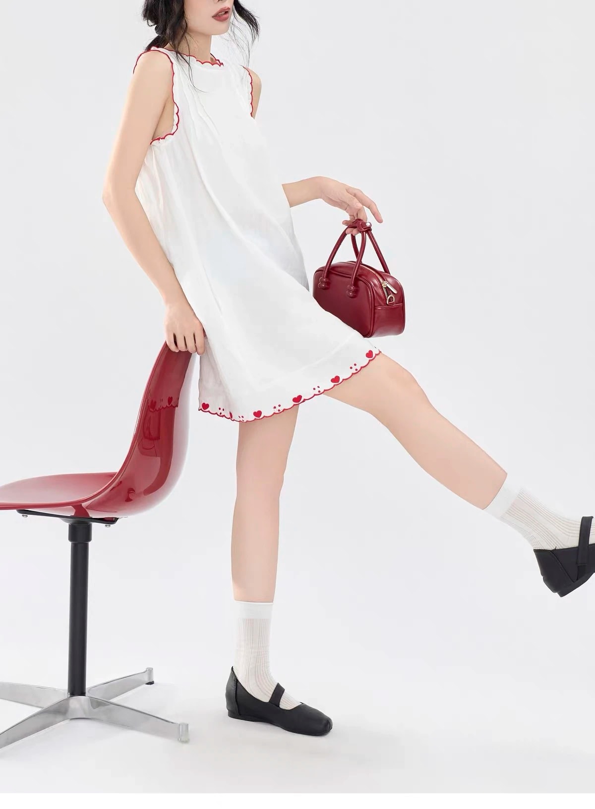 Side view of the Lucie Dress leaning on a red chair, the heart hem above the knee.