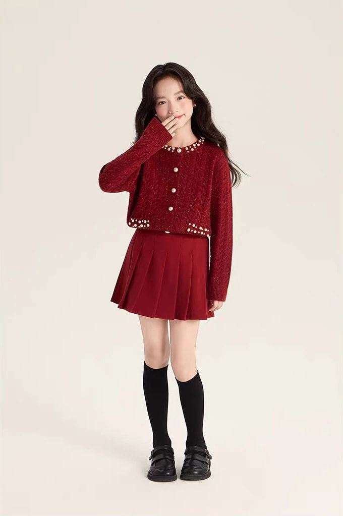 Tampak depan seluruh badan anak perempuan memakai Vivienne Cardigan yang dikancing, dengan rok lipit dan kaus kaki selutut.