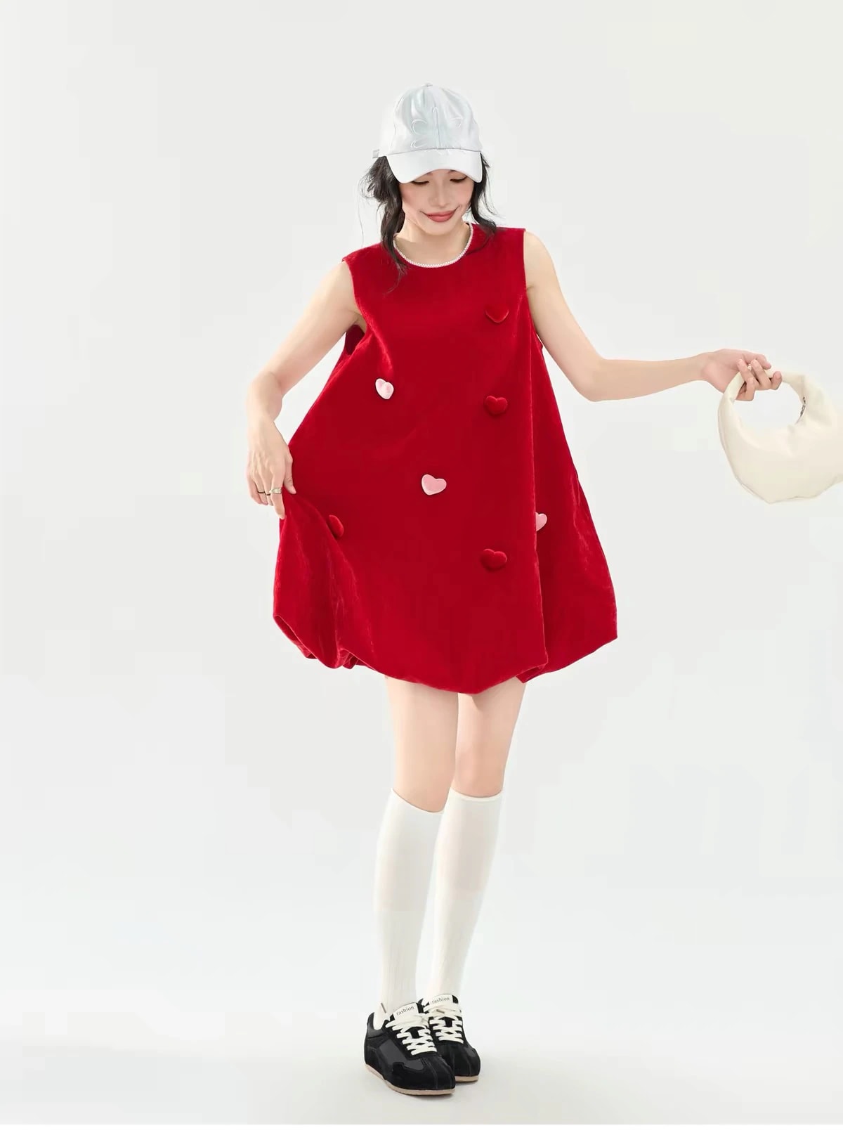 A woman in the red velvet Cerise Dress with pink and red hearts, a Christmas outfit, worn with a white cap and knee socks.