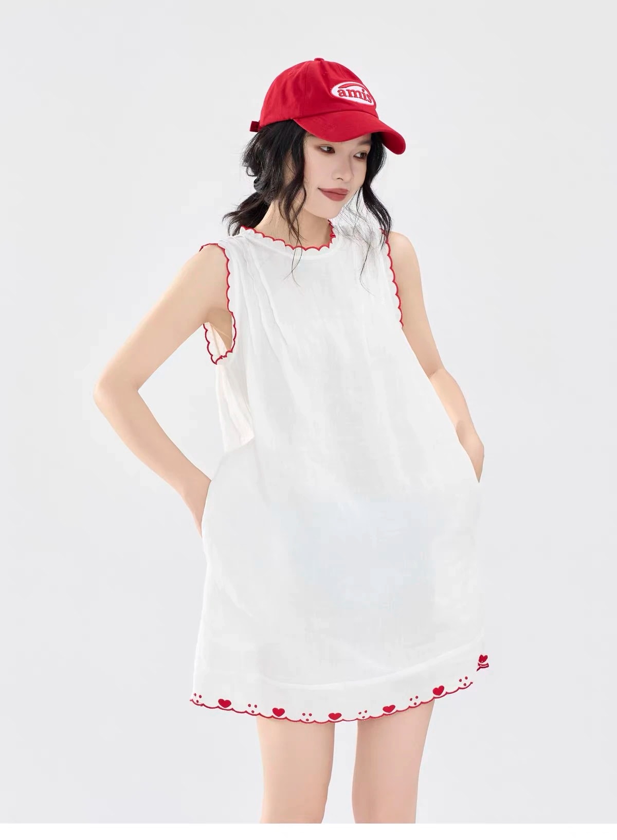 A woman in the white Lucie Dress with red scalloped trim, a Christmas outfit, hands in the side pockets.