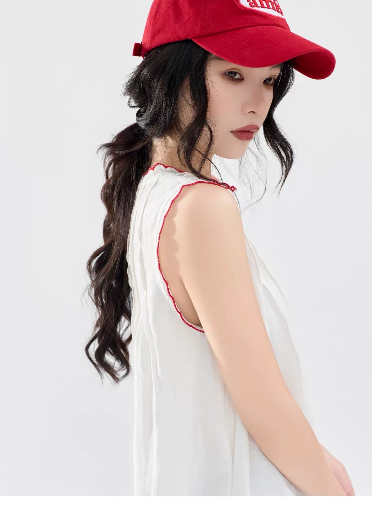 Side profile in the Lucie Dress with a red cap, showing the red scalloped armhole and soft shoulder pleats.